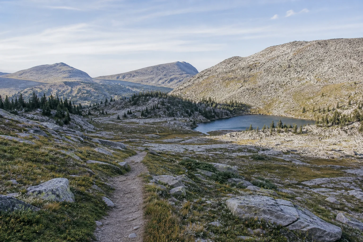 Alpine footpath leading past a small lake beneath pale quartzite ridges
